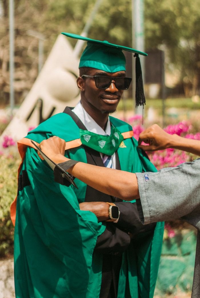 Mastering the First Impression: Your intriguing post title goes here A young male graduate in green cap and gown receiving help outdoors during a sunny day.