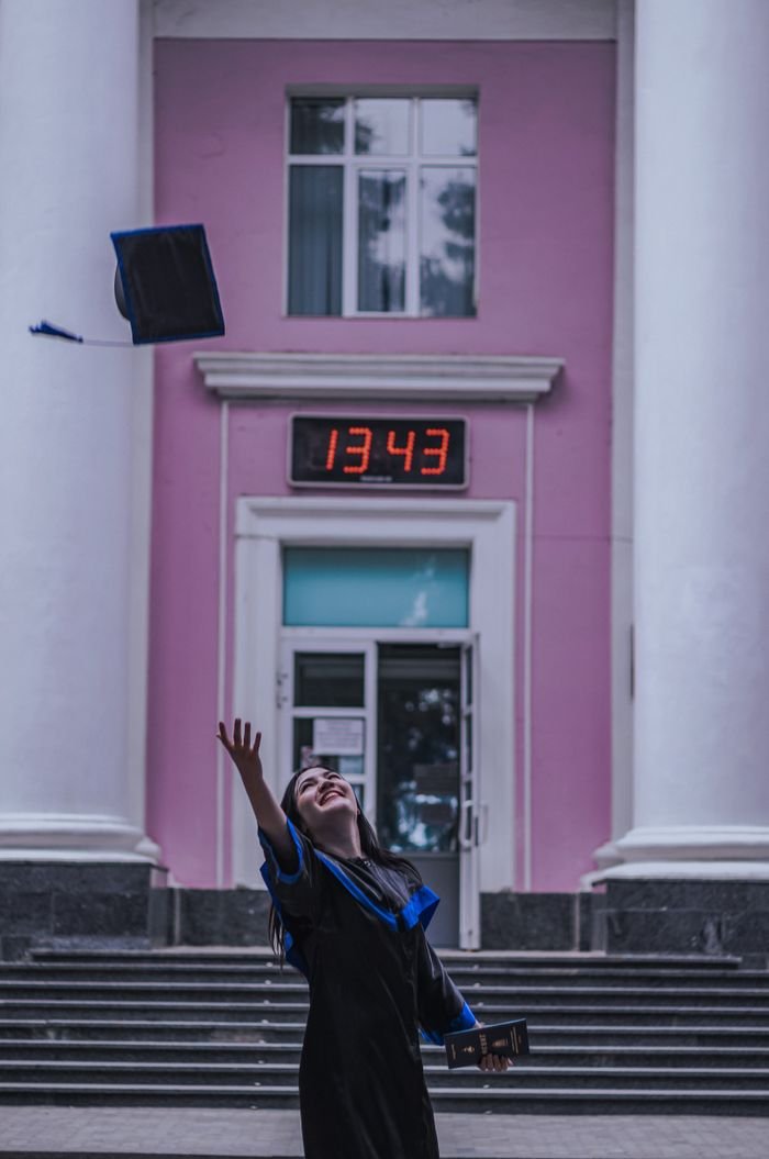 Crafting Captivating Headlines: Your awesome post title goes here Young woman throws graduation cap in joy outside a university entrance.